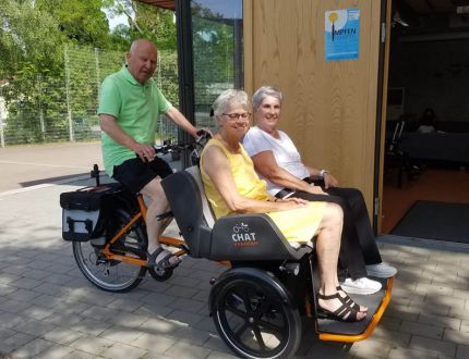 Zwei Seniorinnen sitzen in einem Lastenrad, das von einem Mann gefahren wird.