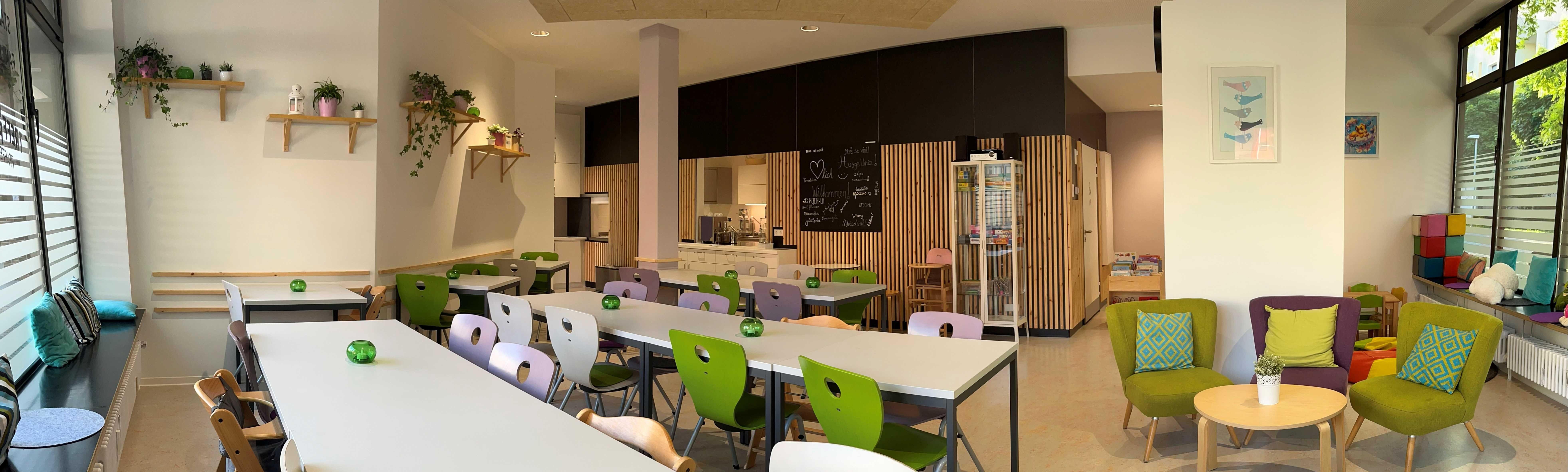 Ein großer Raum mit Theke, Esstischen und Stühlen, weiteren Sitzecken und einer großen Spielelecke für Kinder.